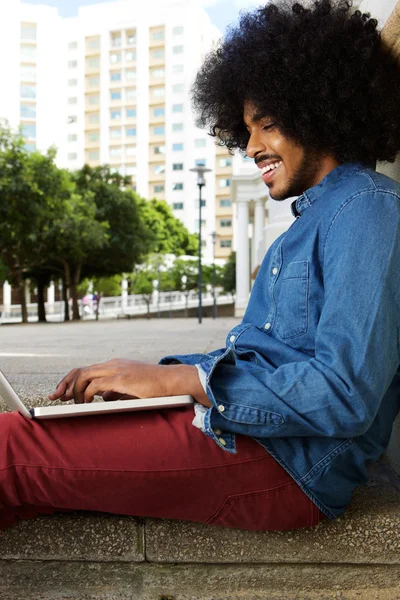 Jeune homme avec afro dactylographier sur ordinateur portable à l'extérieur dans la ville — Photo