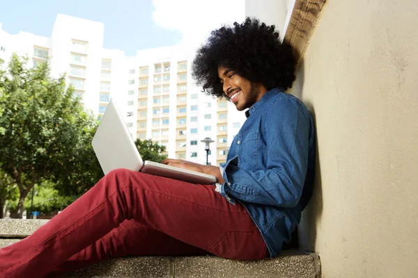 Étudiant souriant assis dehors travaillant sur un ordinateur portable — Photo