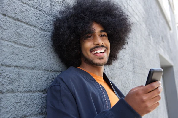 Улыбающийся молодой человек с афро с помощью мобильного телефона — стоковое фото