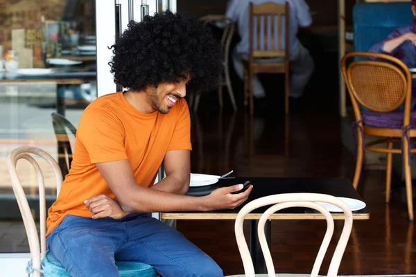 Uśmiechający się młody człowiek przy użyciu telefonu komórkowego w kawiarni — Zdjęcie stockowe