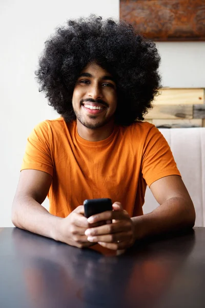 Sonriente hombre afroamericano sentado en casa con teléfono móvil — Foto de Stock