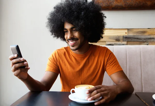 Feliz joven sentado con una taza de café y teléfono móvil —  Fotos de Stock