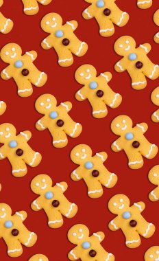 Kırmızı zemin üzerinde şekerleme ve şekerle süslenmiş bebekler şeklinde lezzetli zencefilli Noel kurabiyelerinin dikey deseni