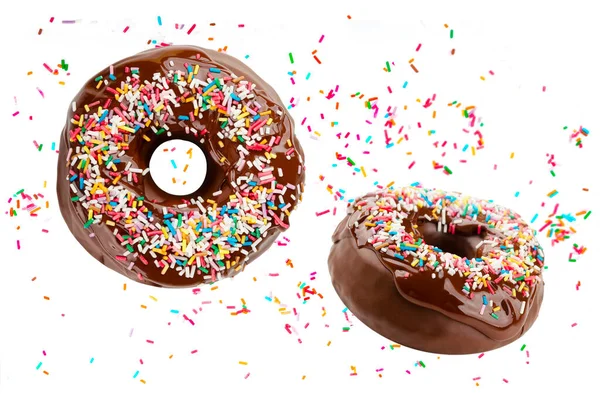 Birçok donut çikolata şekeriyle kaplı ve beyaz arka planda izole edilmiş renkli parçacıklarla süslenmiş bir şekilde uçar. Komik ve lezzetli çörekler.