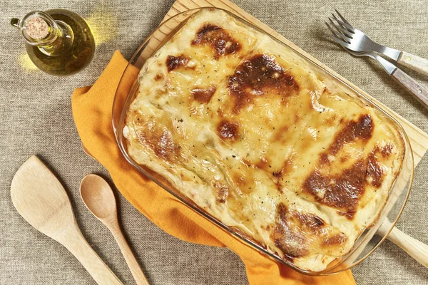 Eritilmiş peynir ve graten ile taze pişmiş lazanya ahşap bir spatulayla servis edilir ve kırsal bir masada zeytin yağıyla yapılır.