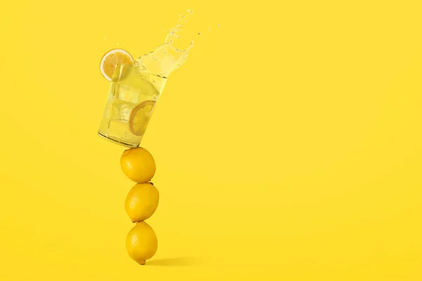 Serinletici bir bardak limonata dengede duran birkaç limonun üstünde ve düşmek üzere. Sarı arkaplanda boşluk kopyala. Sağlıklı, organik, detoks, vejetaryen ve vejetaryen içeceği. Yaz zamanı.