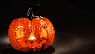 Seramik balkabağı, içinde mum olan ürkütücü bir yüzle Cadılar Bayramı için fener gibi parlayan siyah arka planda fotokopi alanı ile birlikte.