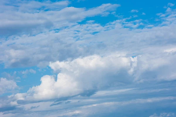 Large clouds and storm clouds close-up against a blue sky. White clouds are mixed with thunderclouds.