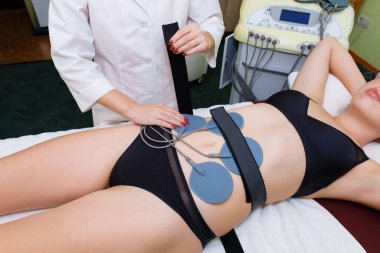 Genç bir kadının karın kaslarına miostimülasyon elektrotları yerleştirilir. İnce bir kadın kas miyostimülasyonu geçiriyor..