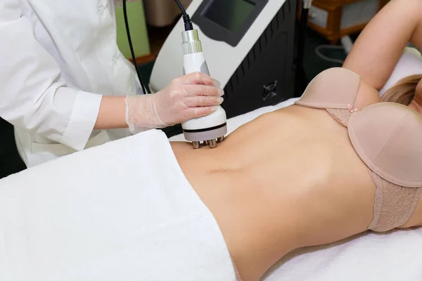Spa salonunun güzellik uzmanı selüloit çıkarmak için karın kaslarını kaldıran genç bir kadının prosedürünü uyguluyor. Donanım kozmetolojisi, kilo kaybı.