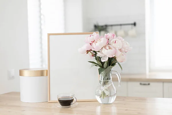 Moldura vertical e maquete caixa de presente em uma mesa de madeira na cozinha. Vaso de vidro com um buquê de peônias rosa e uma xícara de café preto. Estilo escandinavo interior. — Fotografia de Stock