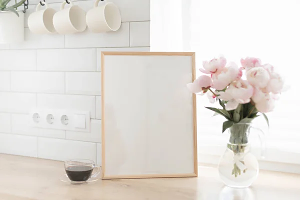 Moldura vertical mockup em uma mesa de madeira na cozinha. Vaso de vidro com um buquê de peônias rosa e uma xícara de café preto. Estilo escandinavo interior. — Fotografia de Stock