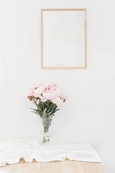 Vertikale Rahmenattrappe auf einem Holztisch in der Küche. Glasvase mit einem Strauß rosa Pfingstrosen. Innenraum im skandinavischen Stil. — Stockfoto