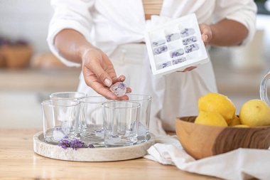 Taze lavantalı limonata. İkinci adım, yaz kokteyli yapmak için gerekli malzemeler. Kullanıcı rehberi. Kız mutfakta bir içki hazırlıyor. Donmuş buzu bardaklara koyar.