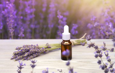 Şişede lavanta yağı ve gri ahşap masadaki damlalar. Yatay yakın plan.