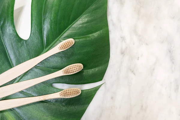 Cepillo de dientes de bambú sobre una mesa con espacio para copiar sobre un fondo de mármol. Composición de estilo de la puesta plana con hojas de monstera . — Foto de Stock