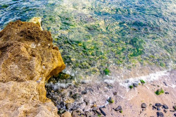 Våg rullar på klipporna i sandiga kust — Stockfoto