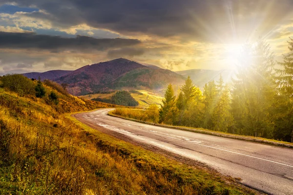 Strada di montagna vicino alla foresta di conifere con cielo nuvoloso a soli — Foto Stock