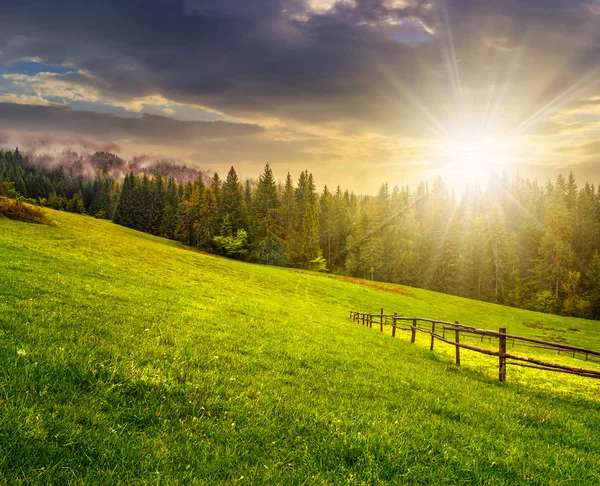 Fence on hillside meadow in mountain at sunset — Stock Photo, Image