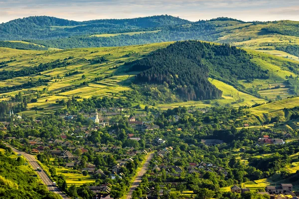 Vesnice na kopci louku s lesa v horách v sunrise — Stock fotografie