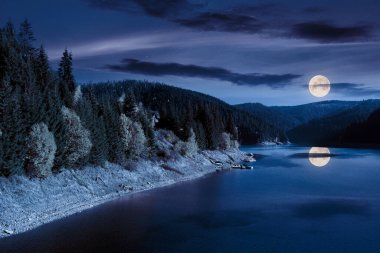 mountain lake in autumn season at night. beautiful countryside scenery in full moon light. blue sky with fluffy clouds reflecting on the water surface clipart