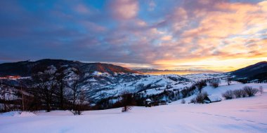Gündoğumunda kış dağı manzarası. Karla kaplı tepelerdeki ağaçlar ve tarlalar. Dramatik bir gökyüzünün altında bulutlu bir tepe. Güzel Karpatlar kırsalları