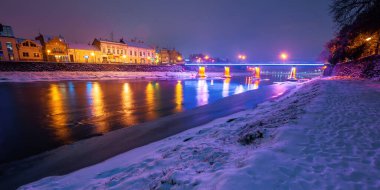Uzhhorod, Ukrayna - 26 DEC 2016: Yılbaşı gecesi eski bir kasaba. Nehir kenarındaki güzel şehir manzarası. Seddin üzerinde kar var. Köprü ve fenerler uzakta parlıyor