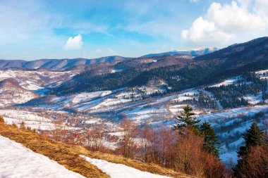 Güneşli bir günde dağlık bir kırsal bölge. Kış sonu manzarası ya da bahar başlangıcı. Tepelerde eriyen karlar ve yapraksız ağaçlar. Uzak vadideki köy. Transcarpathia, Ukrayna