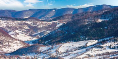 Güneşli bir günde dağlık bir kırsal bölge. Kış sonu manzarası ya da bahar başlangıcı. Tepelerde eriyen karlar ve yapraksız ağaçlar. Uzak vadideki köy. Transcarpathia, Ukrayna