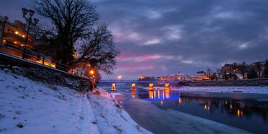 Uzhorod, Ukrayna - 26 Aralık 2016: Şafakta kış şehri. Uzh nehrinin güzel manzarası. Şehir ışıkları suya yansıyor. Toprağa kar yağıyor.