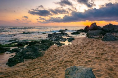 Şafak vakti deniz manzarası. Kumlu sahildeki kayalar. Gökyüzündeki bulutlar. yaz tatili konsepti