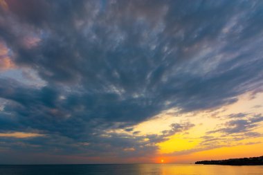 Yazın gün doğumunda dinamik bulutlar. Sarı ve pembe sabah ışığında gökyüzünde kara bulutlar. Dramatik hava koşulları, denizin üzerindeki resim gibi manzaralar.