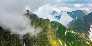 İbnelerin yaz mevsiminde dağ manzarası. Vadinin tepelerinde bulutlar ve karla kaplı harika doğa manzarası. Çimlerdeki ve kayalardaki tepeler. Romanya konseptinin karpatlarını keşfetmek