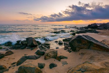 Şafak vakti deniz manzarası. Kumlu sahildeki kayalar. Gökyüzündeki bulutlar. yaz tatili konsepti