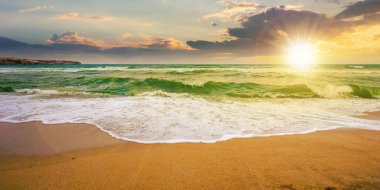 Bulutlu bir gündoğumunda deniz gelgiti. Sabah ışığında kumlu kumsala vuran yeşil dalgalar. Fırtına yaklaşıyor. Yaz tatili konsepti