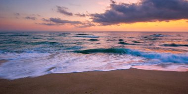 Güneş doğarken dramatik gökyüzü olan deniz plajı. Güzel bir tatil geçmişi. Dalgalar sabah vakti kumda yuvarlanıyor.