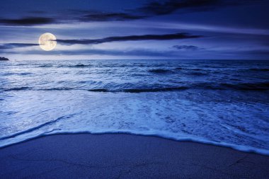 Gece deniz kenarında yaz tatili. Dolunay ışığında güzel bir deniz manzarası. Sakin dalgalar altın kumlu sahili yıkıyor. Gökyüzünde kabarık bulutlar