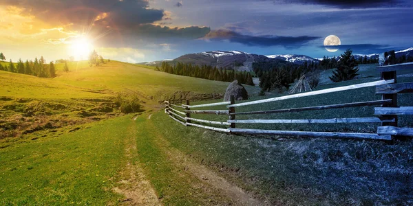 day and night time change concept above rural landscape in spring. path through grassy field. wooden fence on rolling hills. snow capped ridge in the distance. wonderful countryside scenery with sun and moon