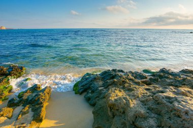 Güneşli bir sabahta deniz manzarası. Denizde yaz tatili. Su, kumlu sahili kayalarla yıkar. Gökyüzünde kabarık bulutlar