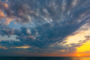 Yazın gün doğumunda dinamik bulutlar. Sarı ve pembe sabah ışığında gökyüzünde kara bulutlar. Dramatik hava koşulları, denizin üzerindeki resim gibi manzaralar.