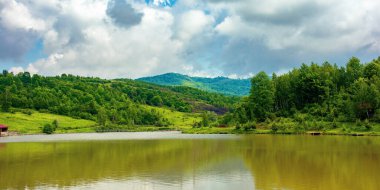 İlkbaharda dağ manzarası arasında göl. Sahilde ormanı olan güzel bir kır manzarası. Gökyüzündeki bulutlar