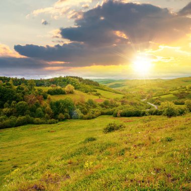 Baharda gün batımında Carpathian kırsalında. Dağdaki güzel kırsal alan. Akşam ışığında ıslak çimenli çayır. Vadiden köye dolambaçlı yollar. Bulutlardaki uzak sırt