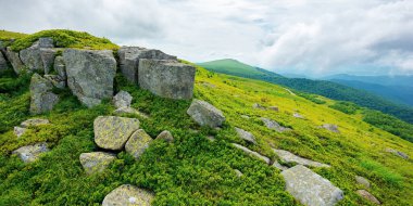 Yazın dağlık alp manzarası. Hava bulutlu. Çimenli tepeler ve çayırlardaki taşlar ve kayalar. Uzaktaki güzel manzara