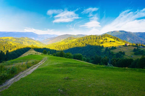 夏日日出时山中的乡村风景 乡间小路穿过长满青草的牧场 蜿蜒而下 一直延伸到遥远的山谷 蓝天上的云彩在远处的山脊上 — 图库照片