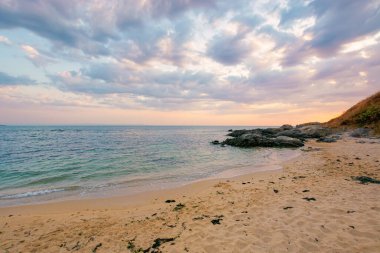 Yaz tatili manzarası gün doğumunda deniz kenarında. Sakin su kumlu sahili yıkar. Ufukta dramatik bulutlar sabah ışığında gökyüzünde