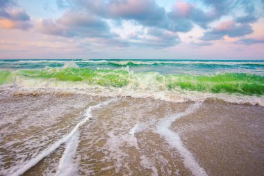 Akşam ışığında bulutlu deniz manzarası. Dalgalar kumlu plaja çarpar. dramatik hava koşulları