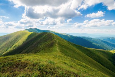 Yazın dağ manzarası. Tepelerdeki çimenli çayırlar bulutlu bir gökyüzünün altındaki uzak tepeye doğru yuvarlanıyor.