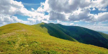 Yazın dağ manzarası. Tepelerdeki çimenli çayırlar bulutlu bir gökyüzünün altındaki uzak tepeye doğru yuvarlanıyor.