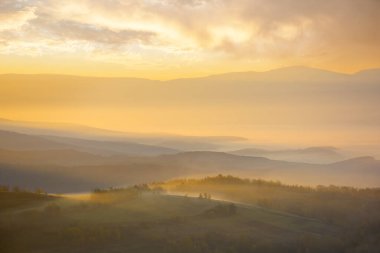 Dağlık kırsal alan, sisli gündoğumunda. Parlayan sisli uzak kırsal vadisiyle muhteşem bir sonbahar manzarası. Sabah vakti tepelerde ağaçlar ve tarlalar