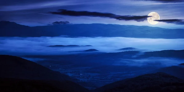 夜の山岳地帯の風景 遠くの霧の谷に転がり込む丘の上の木々や農地です 満月の夜の空の下の尾根 — ストック写真